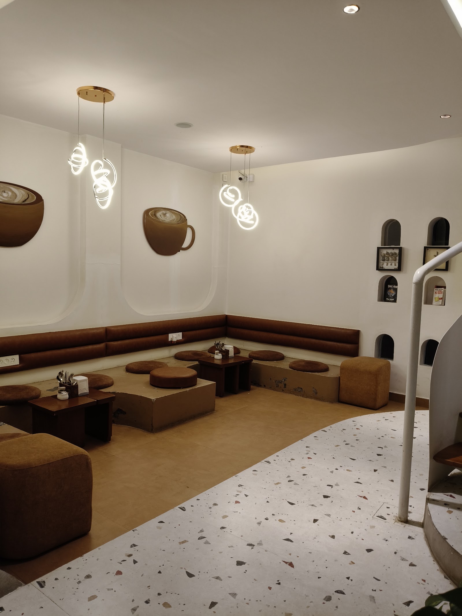 The lounge corner: a long low banquette running two walls, round floor poufs, terrazzo underfoot, and globe pendants hanging over arched niches cut into the plaster.