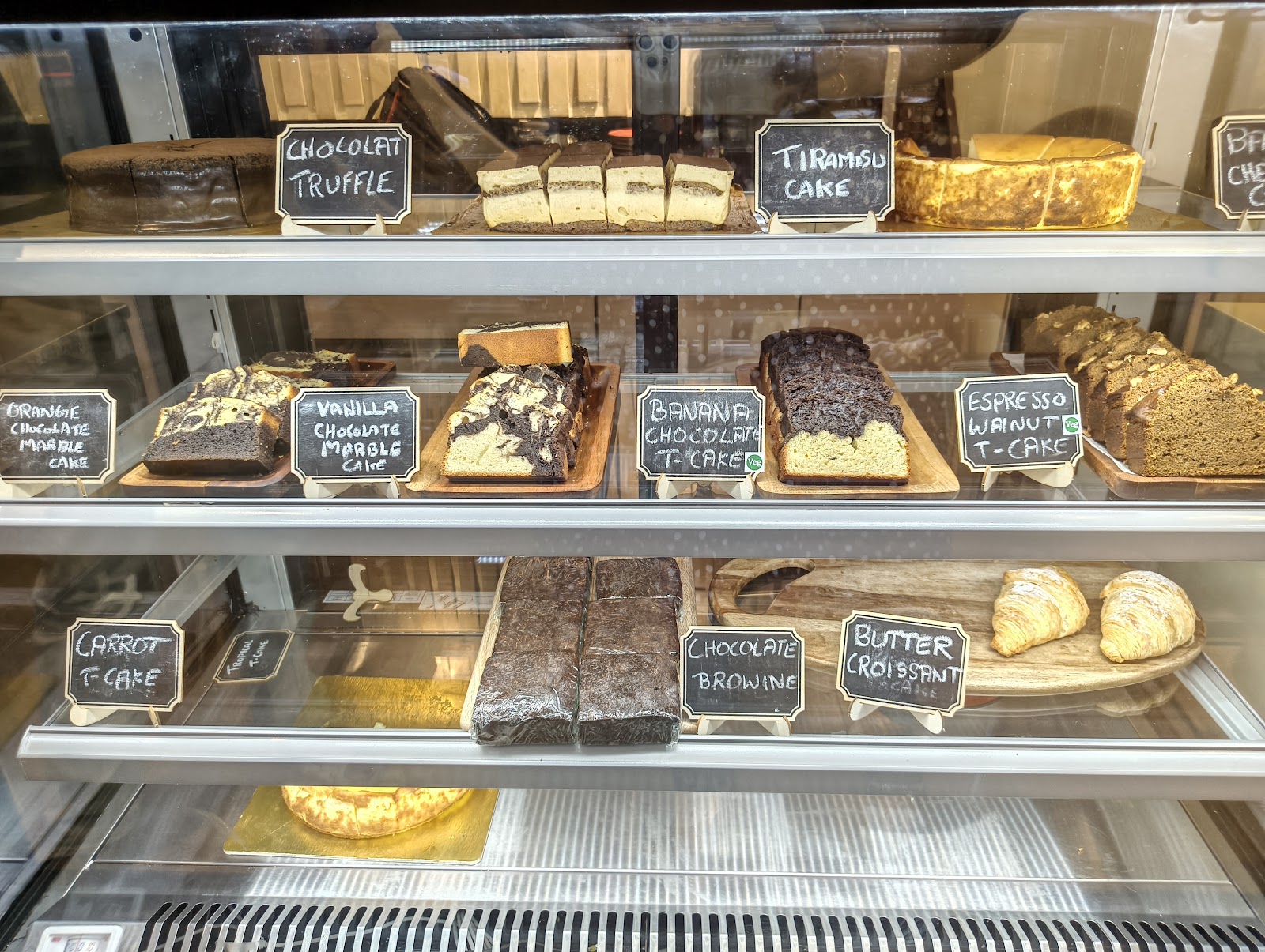 The chilled dessert case beside the counter, its glass shelves lined with cakes and cut slices under small hand-written labels.