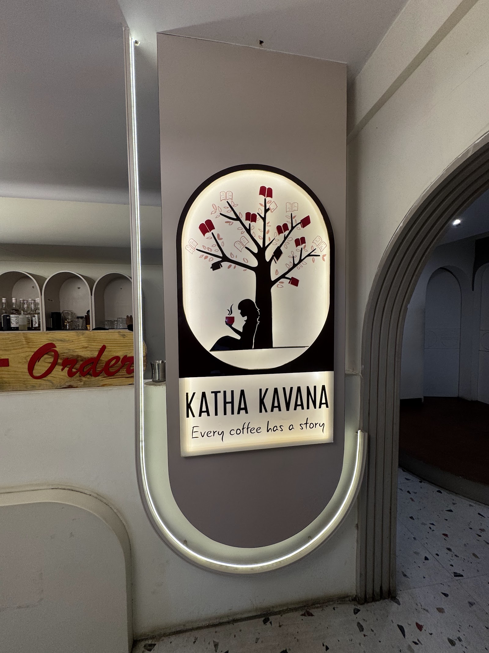 The house sign mounted on a white arched wall inside the cafe, with a rounded arch doorway and terrazzo floor beyond it.