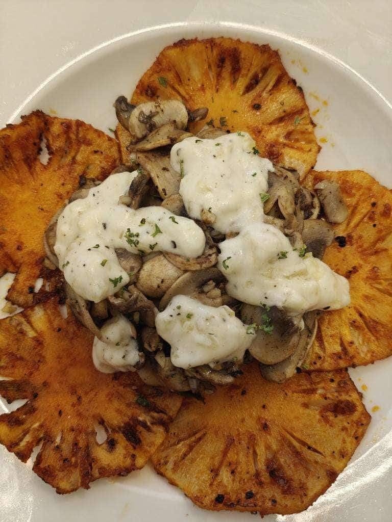 A plate of grilled pineapple rings topped with mushrooms in a cream sauce.