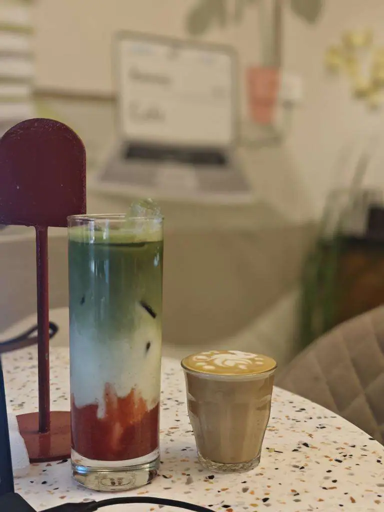 A terrazzo table holding a layered red and green iced drink beside a coffee served in a glass.