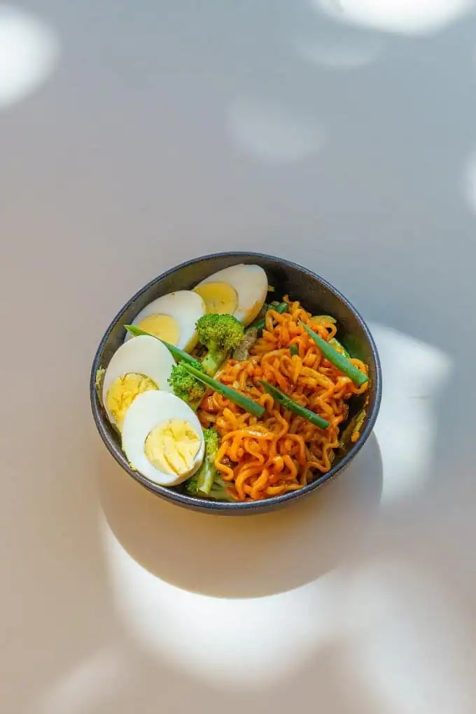 A dark bowl of noodles topped with halved boiled eggs and green beans.