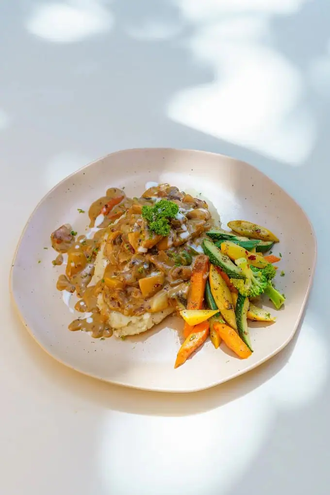 A pale plate of a sauced dish finished with carrot batons and chopped herbs.