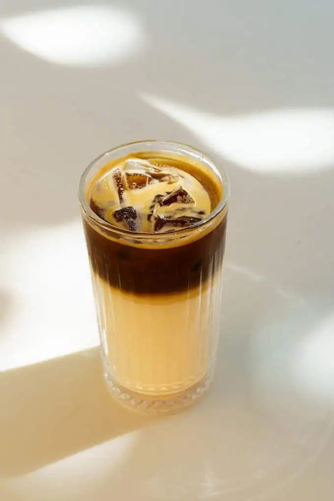 A tall glass of iced coffee in sunlight, dark espresso sitting in a band over pale milk.