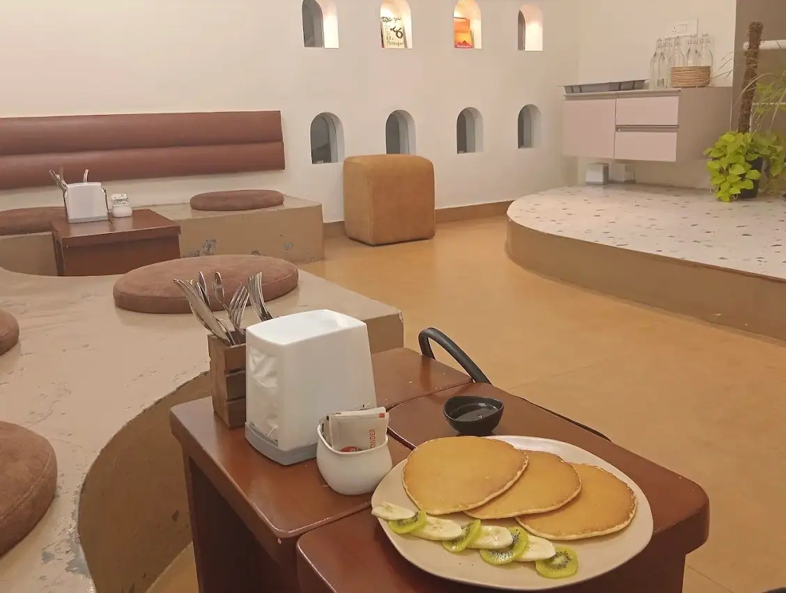 A low lounge table set with a plate of pancakes and sliced lime, cushioned seating around it and arched niches in the wall behind.