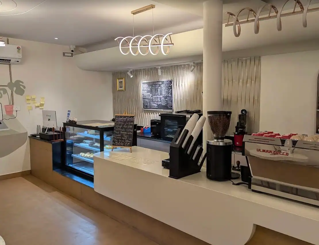 The counter running along a white wall — grinders, a pastry fridge and a rail of hanging hooks above it.