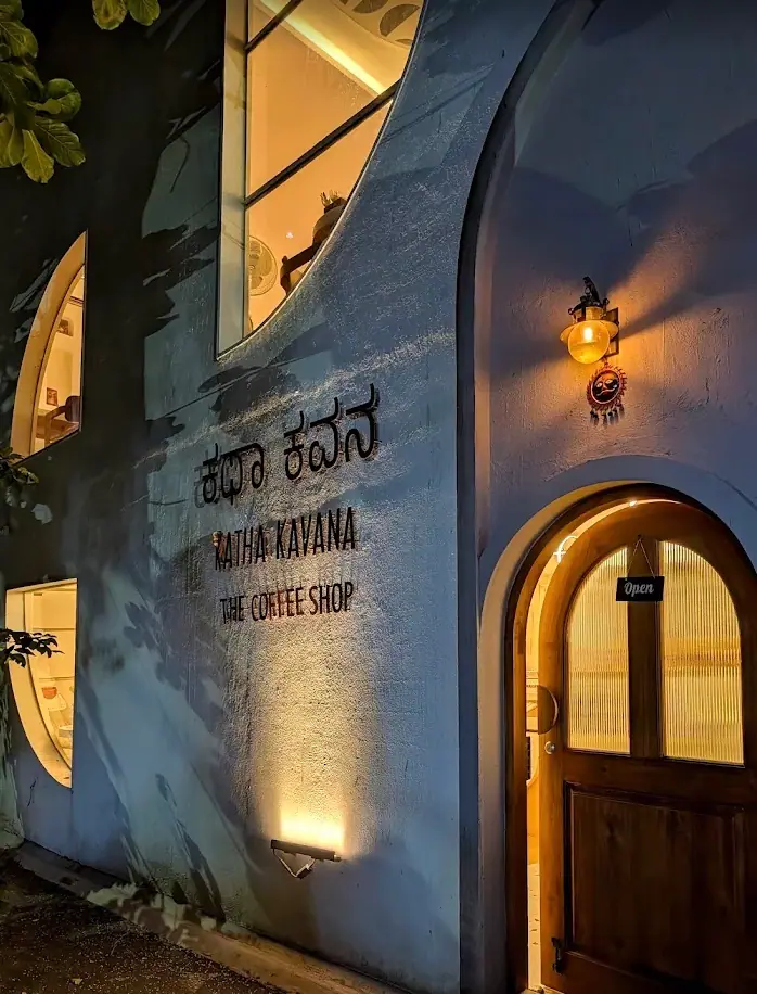 The front of the cafe at dusk: a blue-washed wall, an arched wooden door under a lantern, and the name painted in Kannada and roman script beside it.