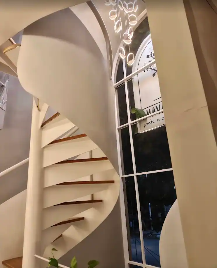 The white sculpted staircase and the tall window beside it, seen from inside.